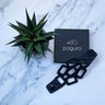 Paguro Upcycle eco friendly chain bracelet in black displayed next to plant and branded box on marble surface