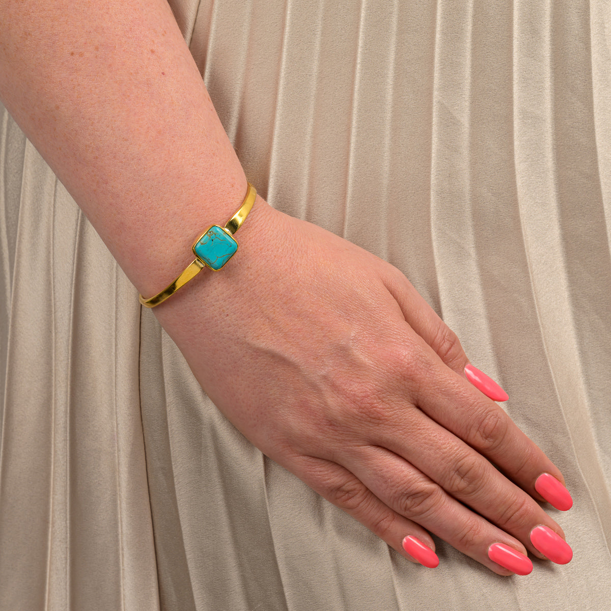 Recycled brass turquoise bangle bracelet worn on wrist with pink nail polish and beige pleated dress