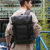 Person wearing a large black backpack in a modern outdoor setting.