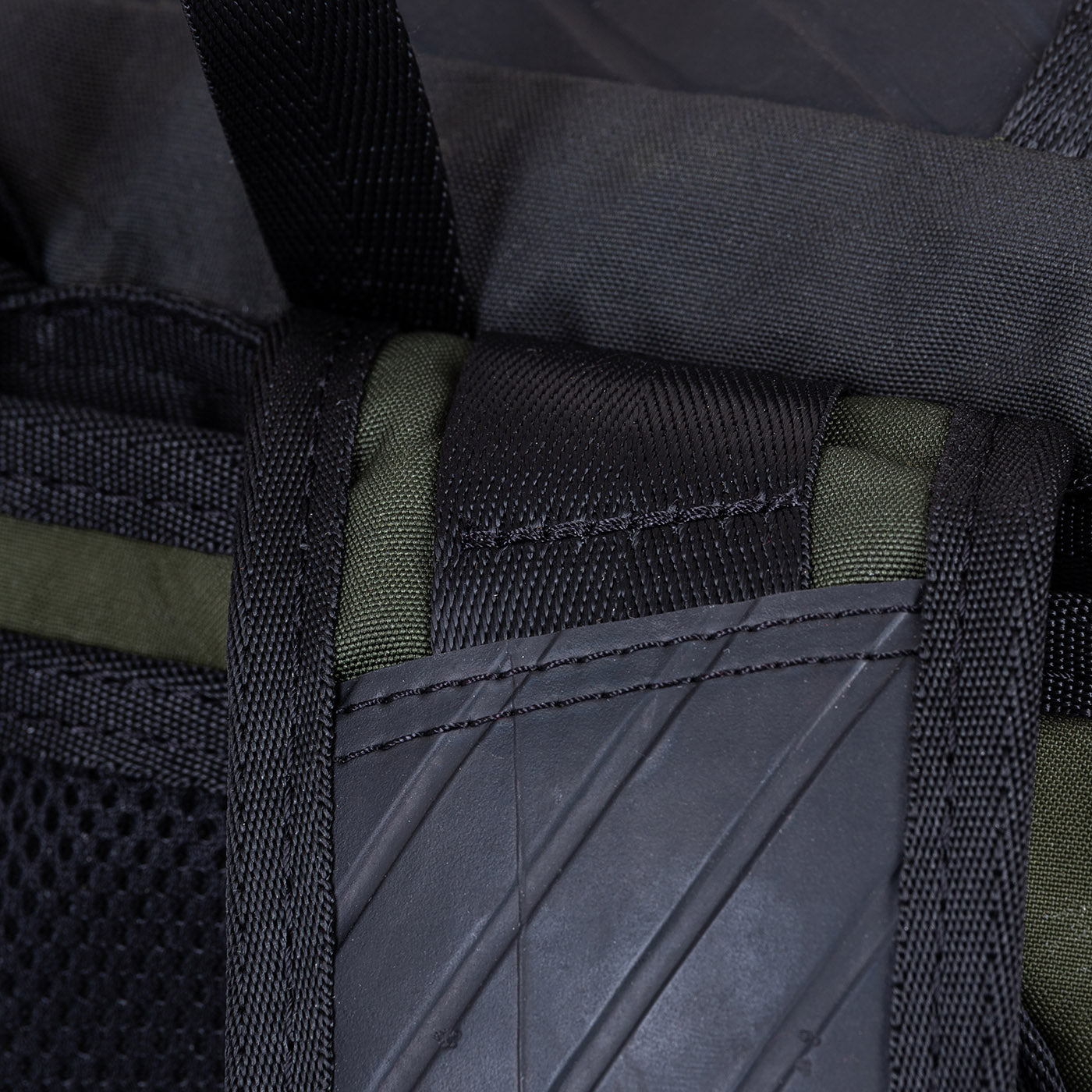 Close-up of a backpack strap and stitching detail in black and green fabric.