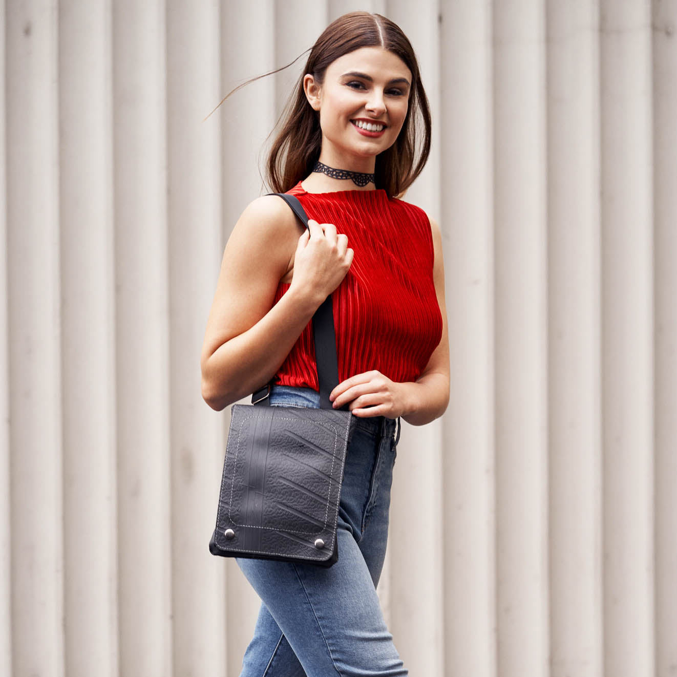 Woman wearing a recycled rubber crossbody bag by Paguro Upcycle with a red top and jeans
