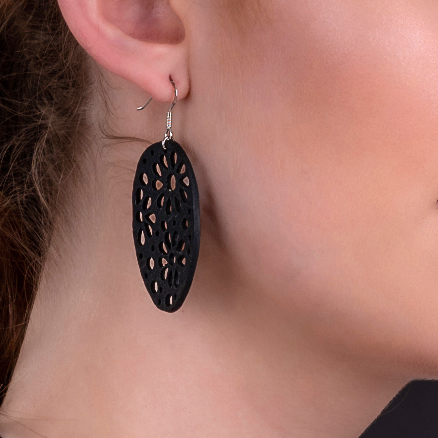 Paguro Upcycle black oval floral cutout recycled rubber earrings UK shown on model with silver hook