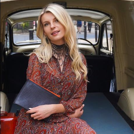 Woman holding a black vegan flat pouch bag from Paguro Upcycle inside a vintage car
