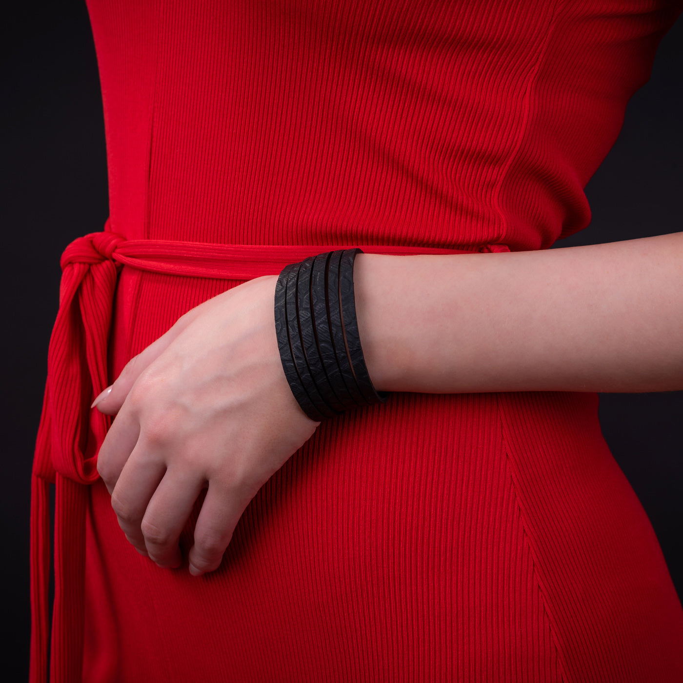 Black recycled rubber bracelet by Paguro Upcycle worn on wrist with red dress background