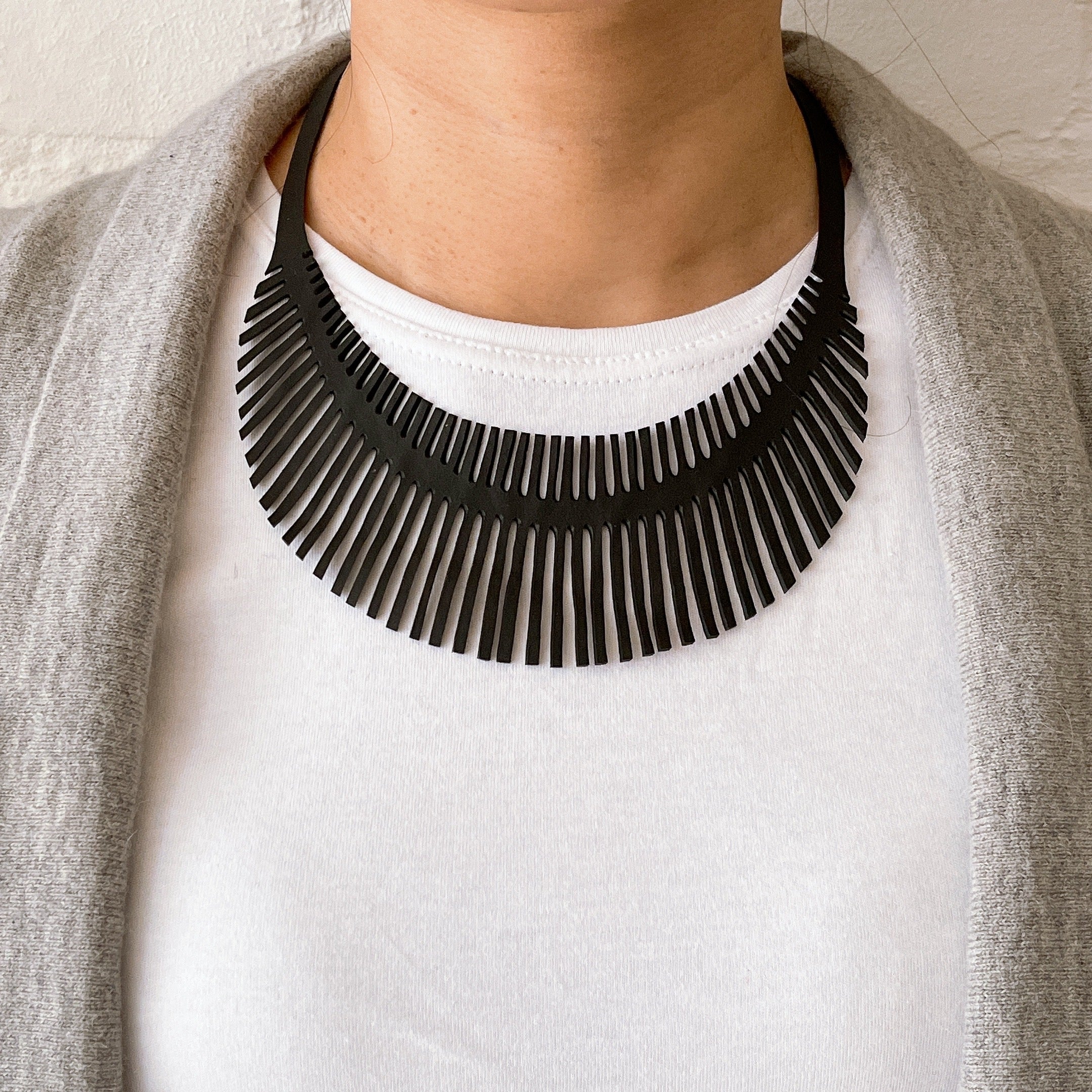 Paguro Upcycle black fringe crescent upcycled inner tube necklace worn over white tee and gray cardigan