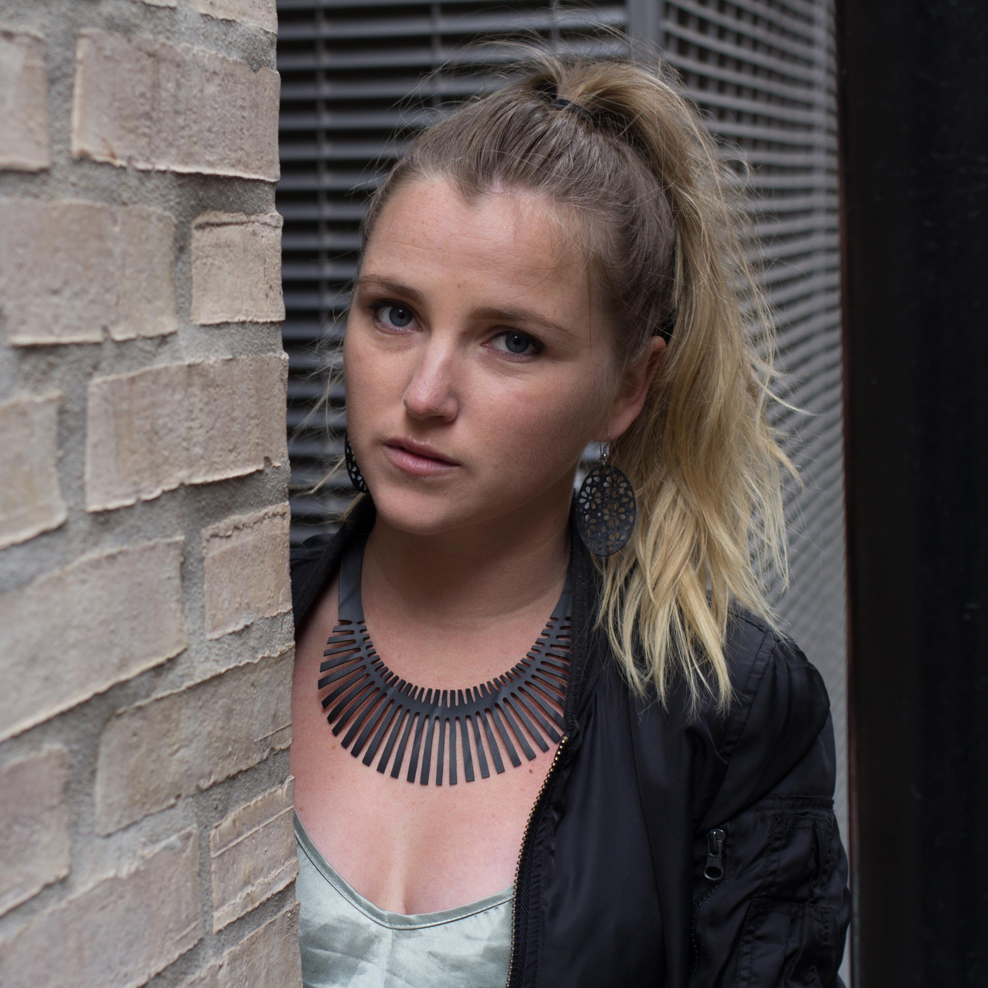 Paguro Upcycle upcycled inner tube necklace on model with ponytail leaning by brick wall