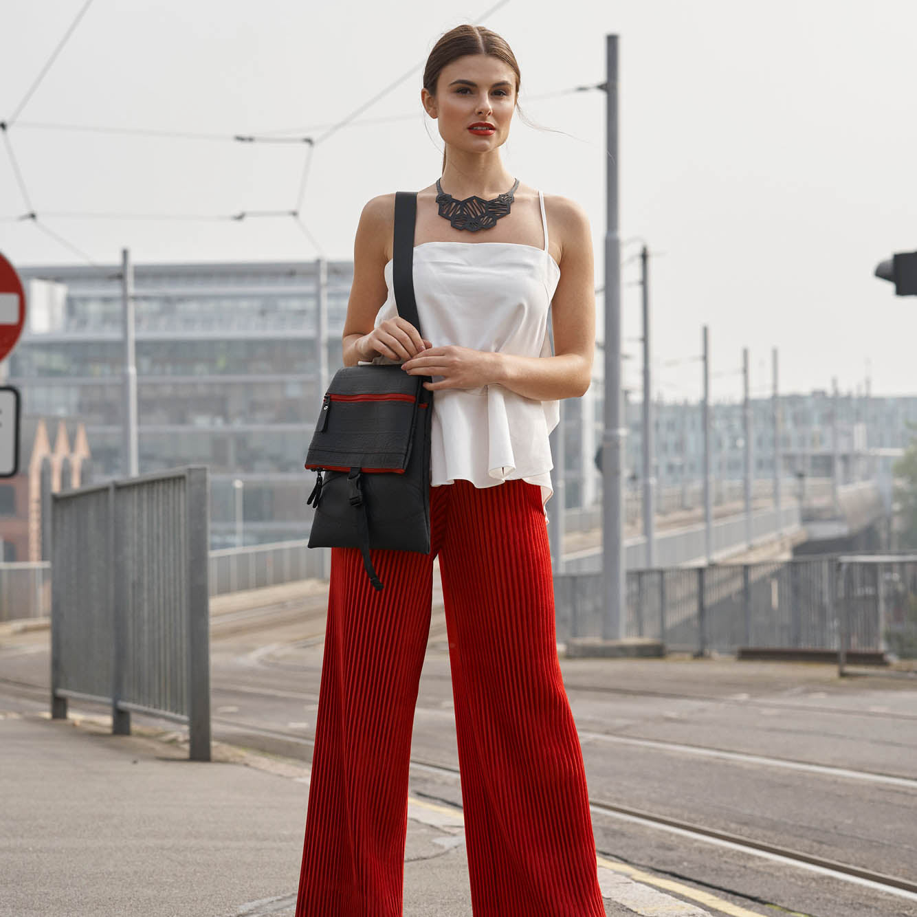 Paguro Upcycle recycled rubber crossbody bag worn by woman with white top and red pants in urban setting