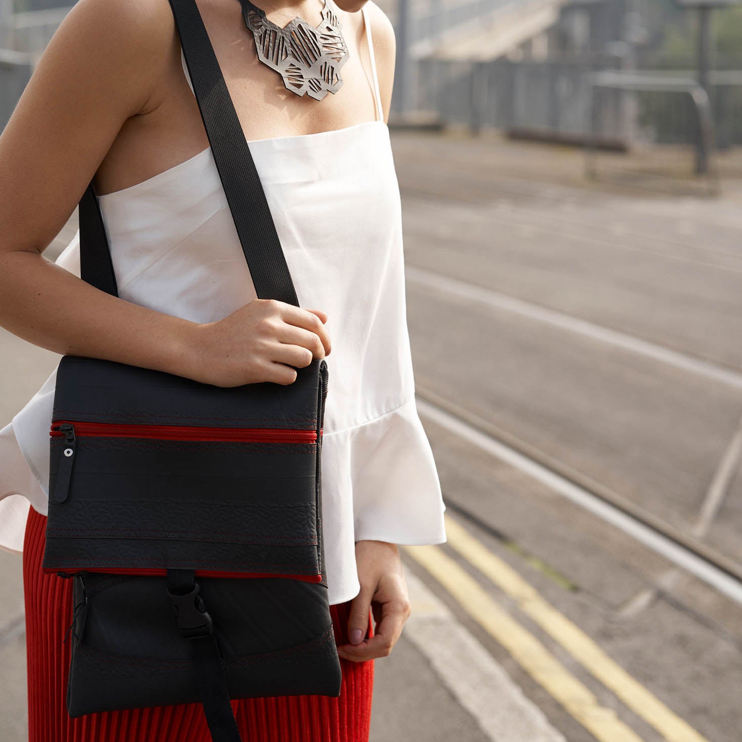Paguro Upcycle recycled rubber crossbody bag with black strap and red zipper worn by woman