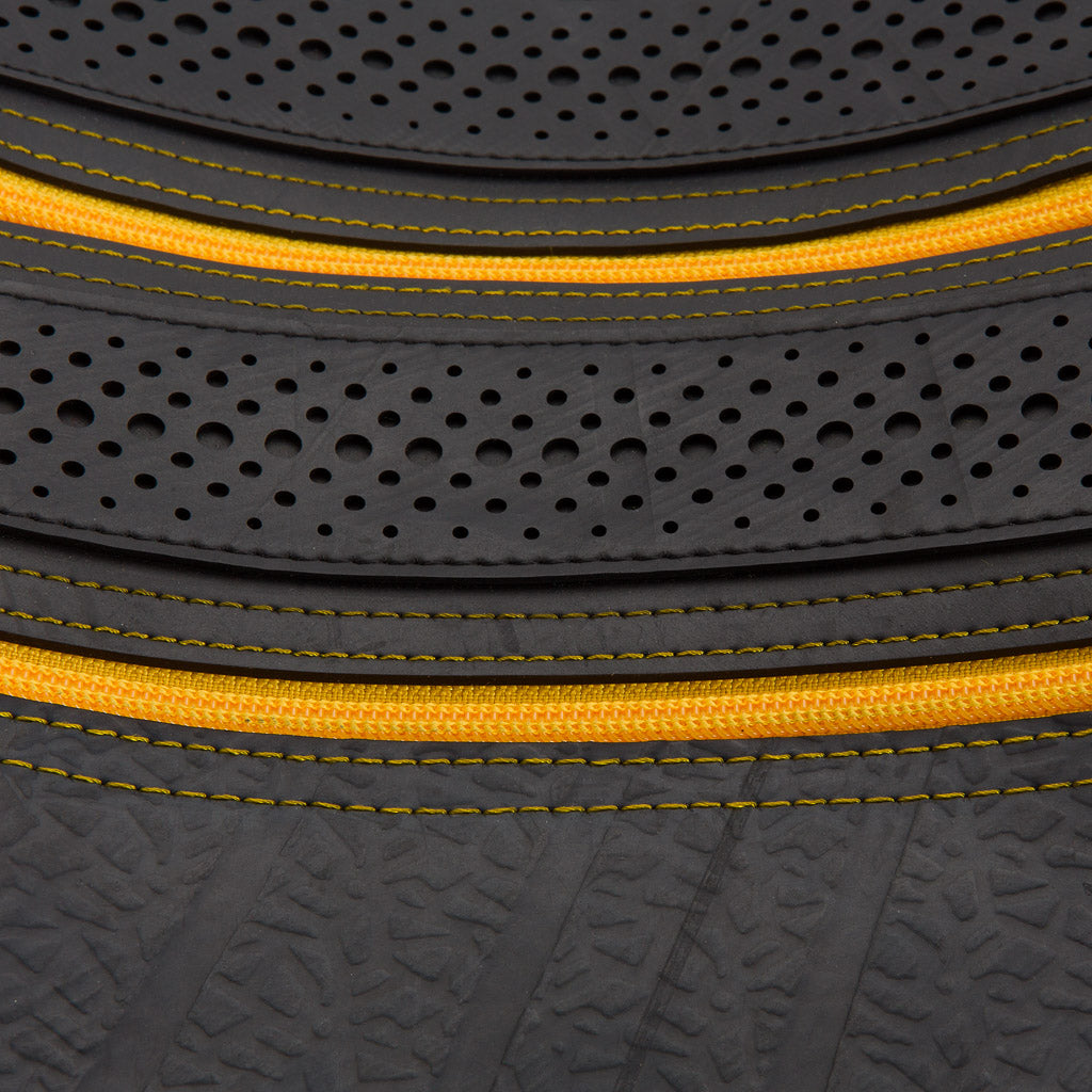 Close-up of Paguro Upcycle recycled rubber vegan handbag featuring perforated details and yellow zipper stitching