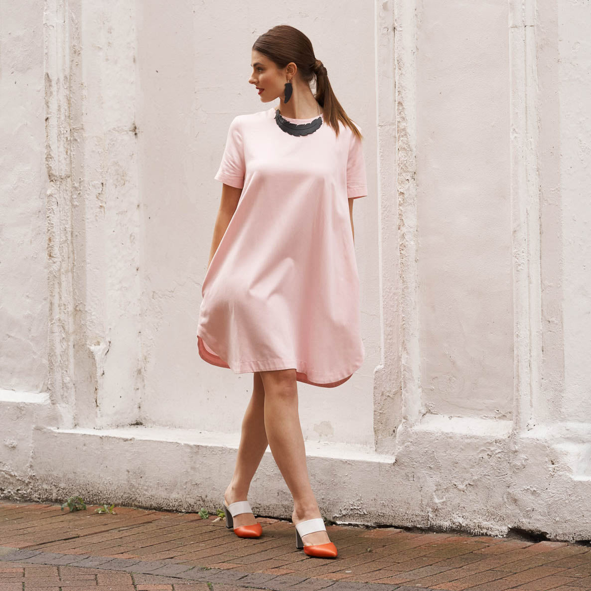 Stylish woman in a pink dress wearing upcycled rubber feather earrings for an eco-friendly look