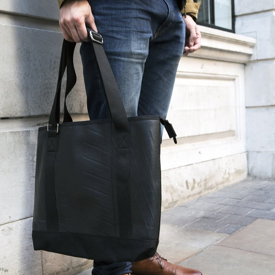 Man holding a black vegan tote bag made from inner tube with adjustable straps outdoors
